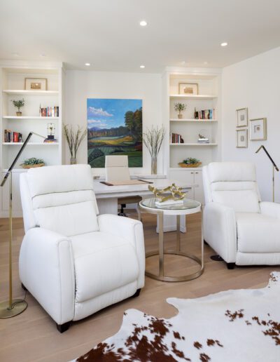 Two white chairs and a cowhide rug in a home office.